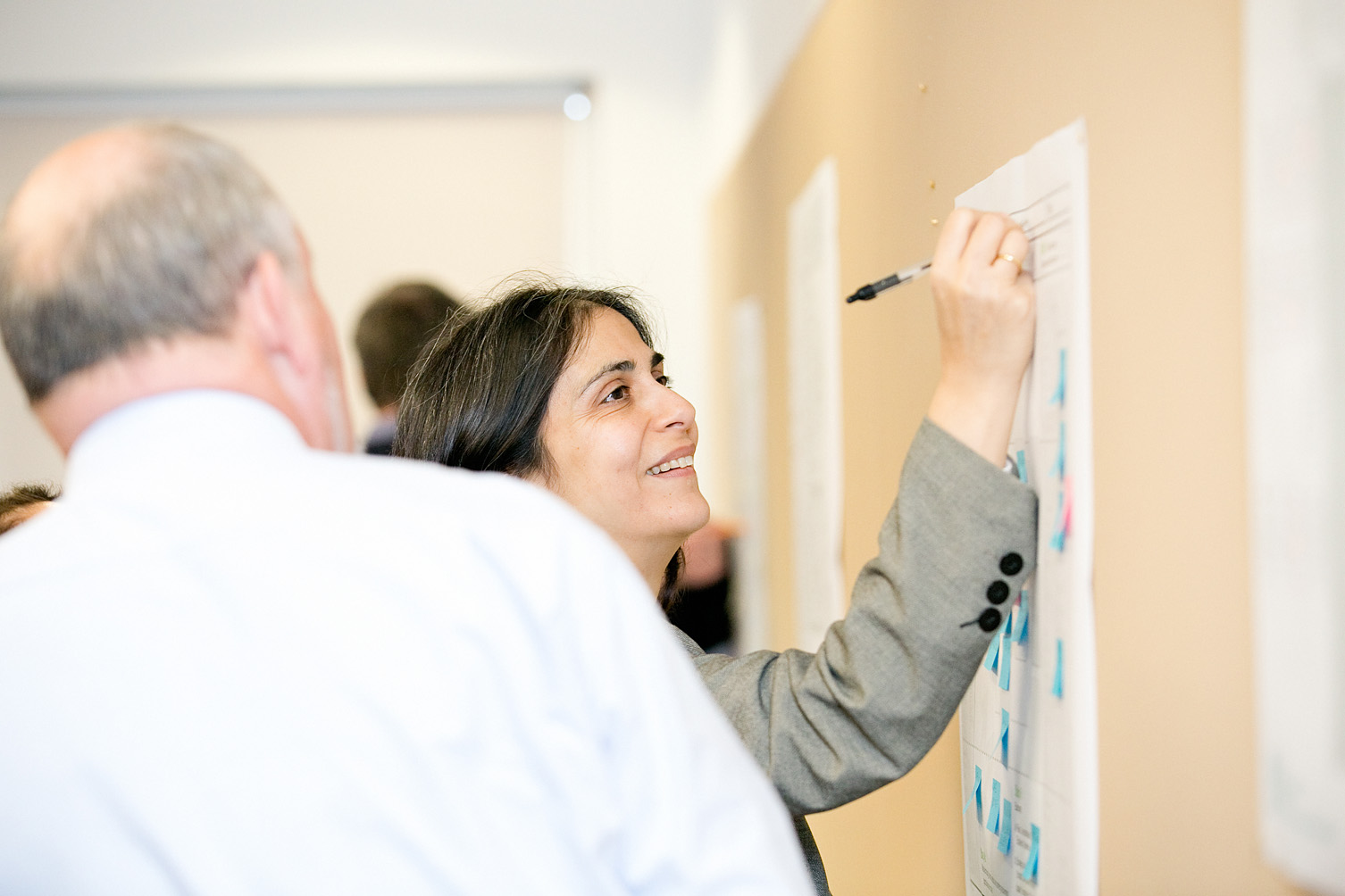 Female with dark hair writing against a poster pinned to a board during a consultancy workshop delivered by IfM Engage.